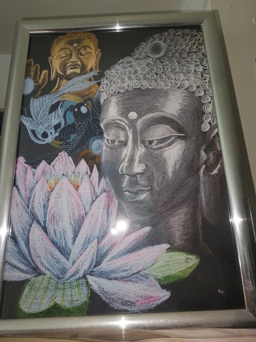 Drawing on black paper of a serene Buddha head in white highlights beside a blooming lotus with pink-tipped petals, with a smaller golden Buddha raising one hand above two koi fish.